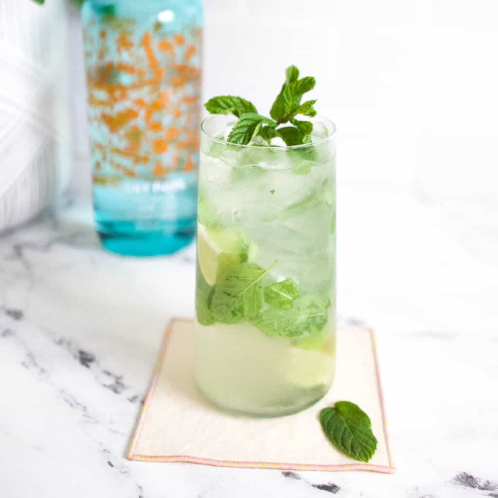 Mojito with a bottle of gin in the background.