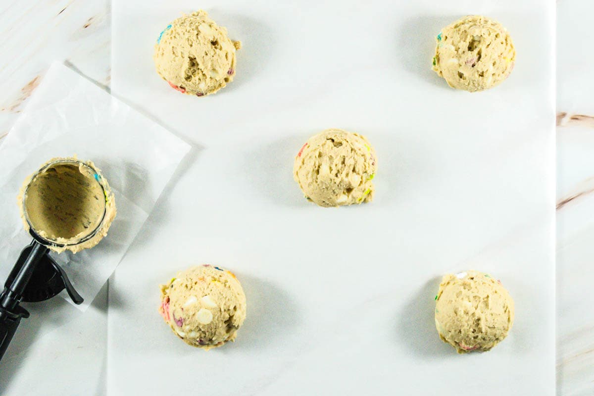 Scoops of Lucky Charms cookie dough with ice cream scoop on parchment paper.