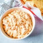 A bowl of Rotel cream cheese dip with a container of corn chips beside it.