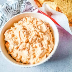 A bowl of Rotel cream cheese dip with a container of corn chips beside it.
