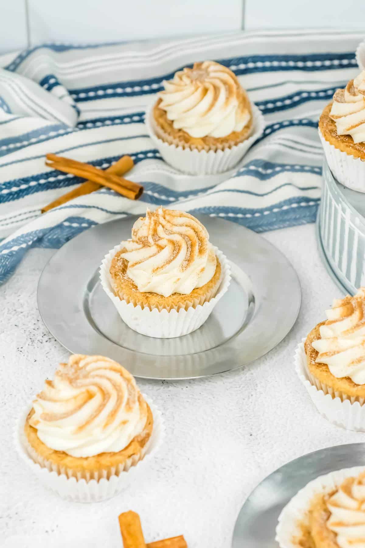 RumChata cupcakes with buttercream frosting and cinnamon sugar topping, blue and white striped kitchen cloth in the background with loose cinnamon sticks.