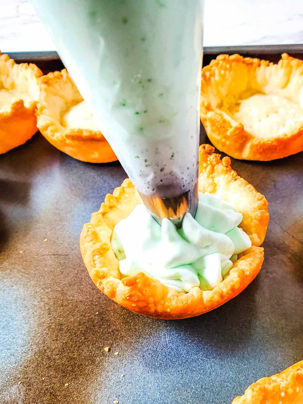 Piping the filling into the baked pie crusts.