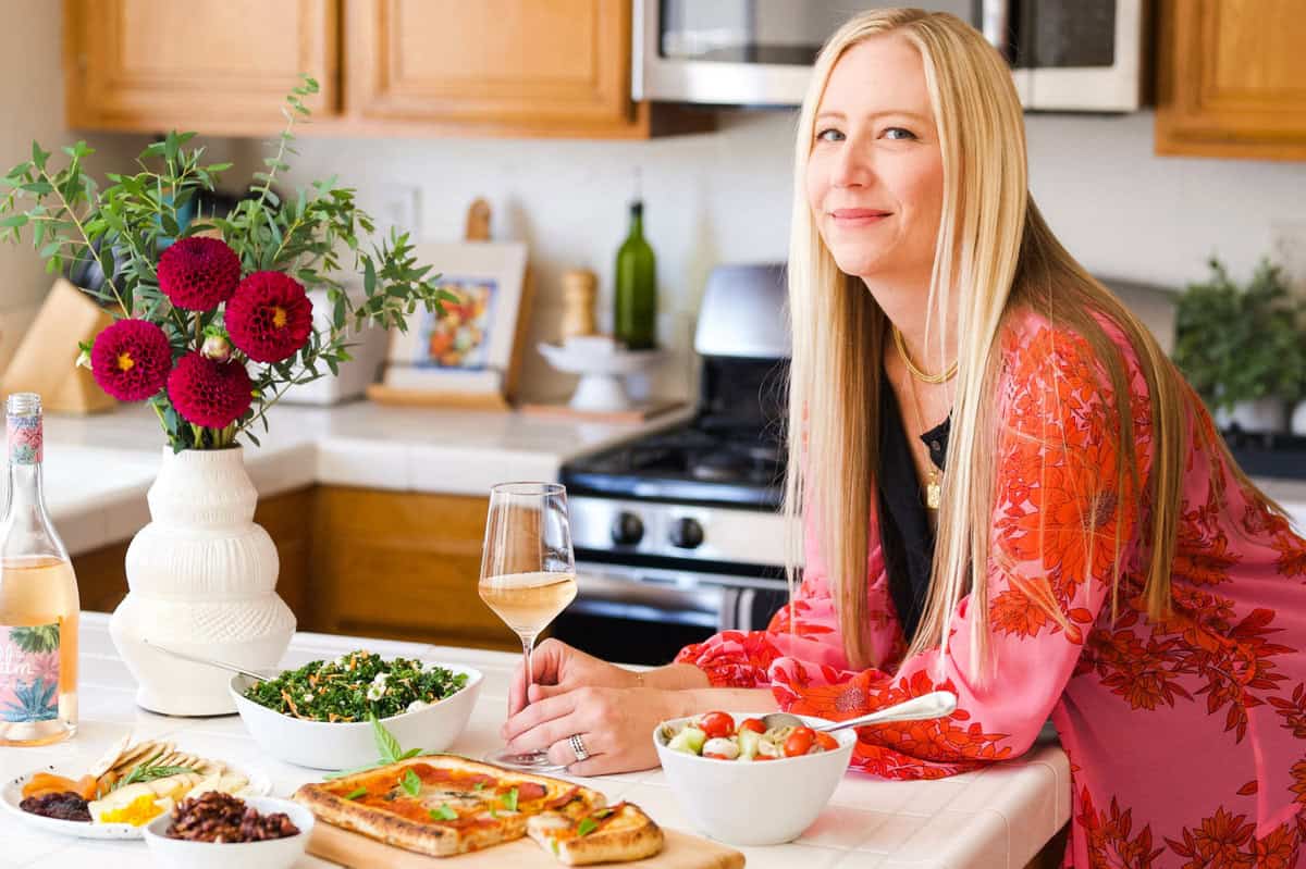 Sharon leaning on the counter with a glass of wine and appetizers for a simple at home party.