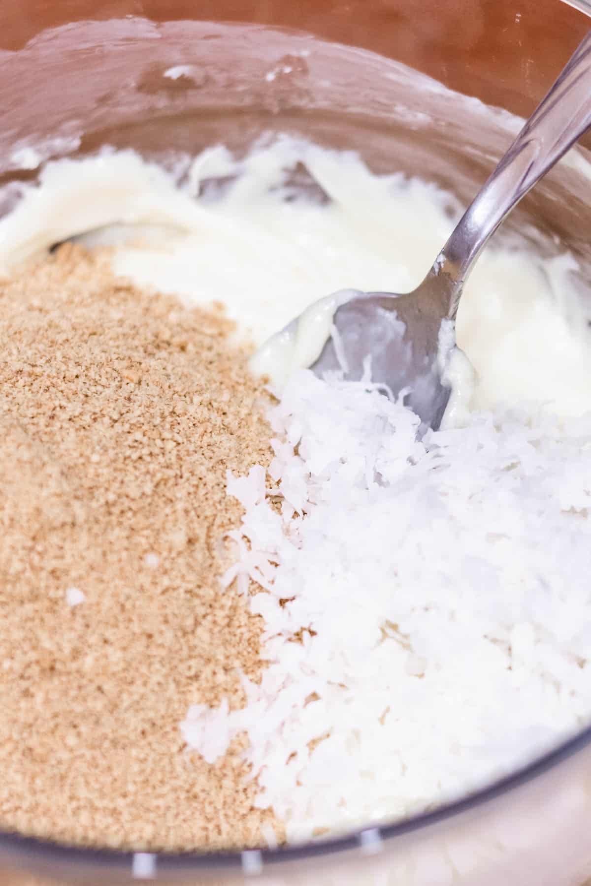 mixing ingredients in bowl Mixing bowl with melted white chocolate chips, cream, shredded coconut, and cinnamon Graham cracker crumbs.