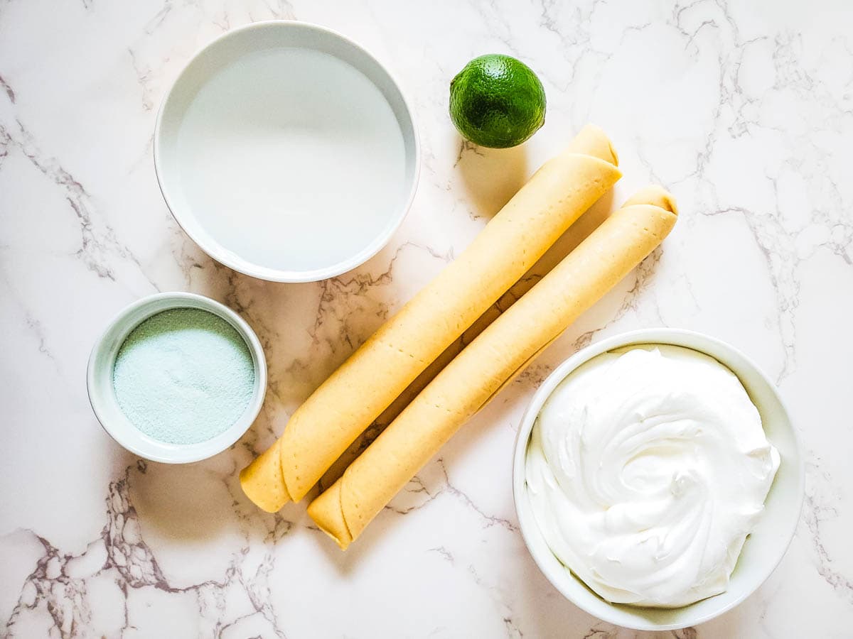 The ingredients you need for making key lime pie bites such as mini pie crusts, lime gelatin package, water, whipped topping, and lime zest.