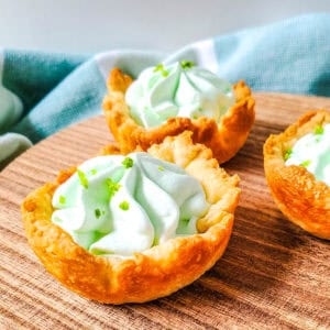 A close up shot of three key lime pie bites on top of a wooden plate.