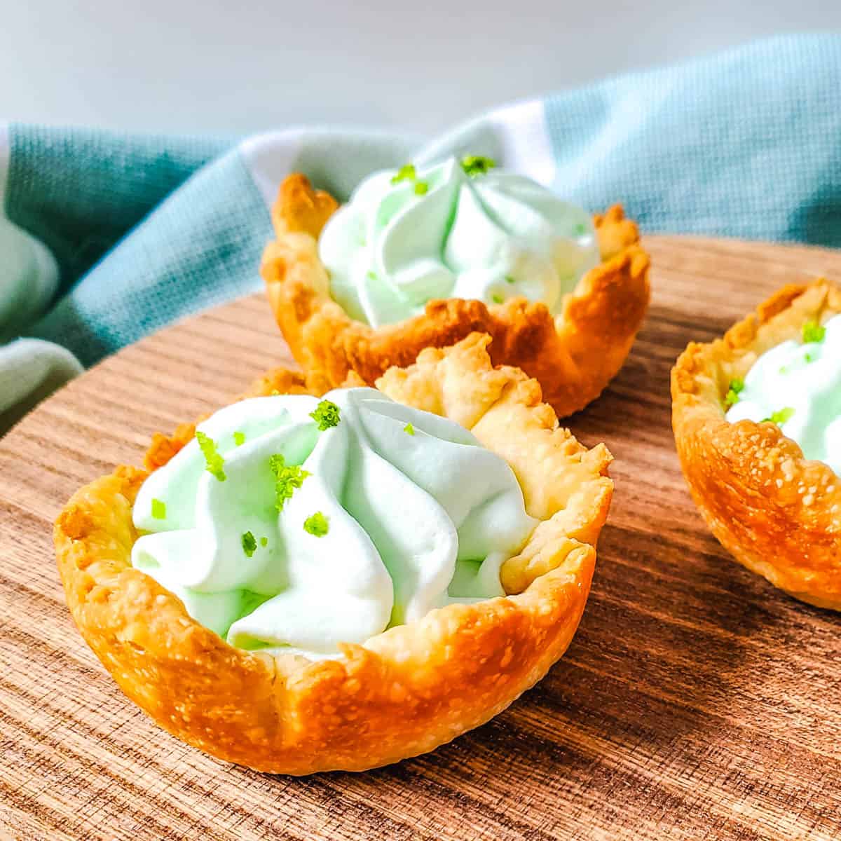 A close up shot of three key lime pie bites on top of a wooden plate.