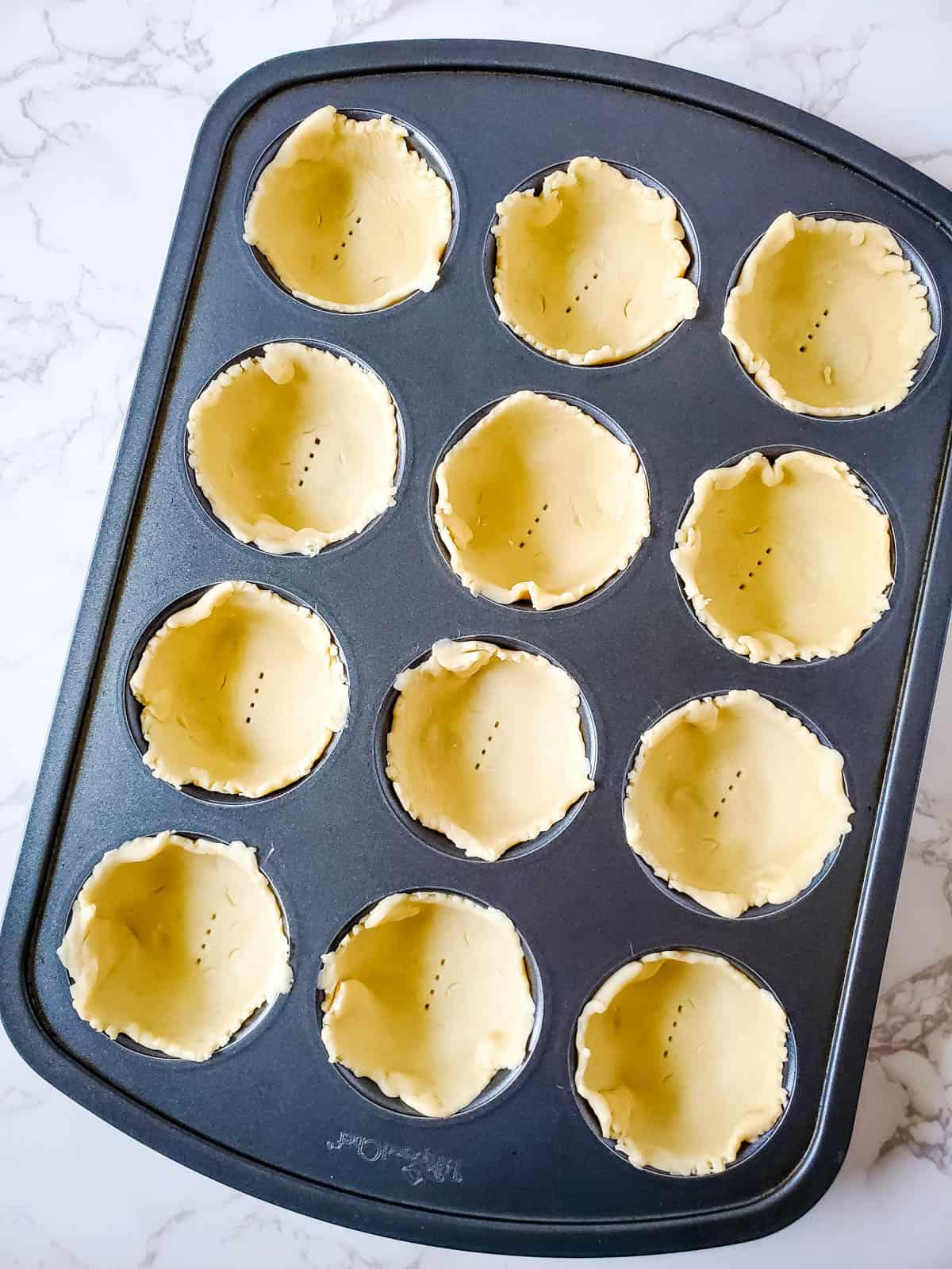 Setting the pie crusts into the 12 muffin tin cavities.