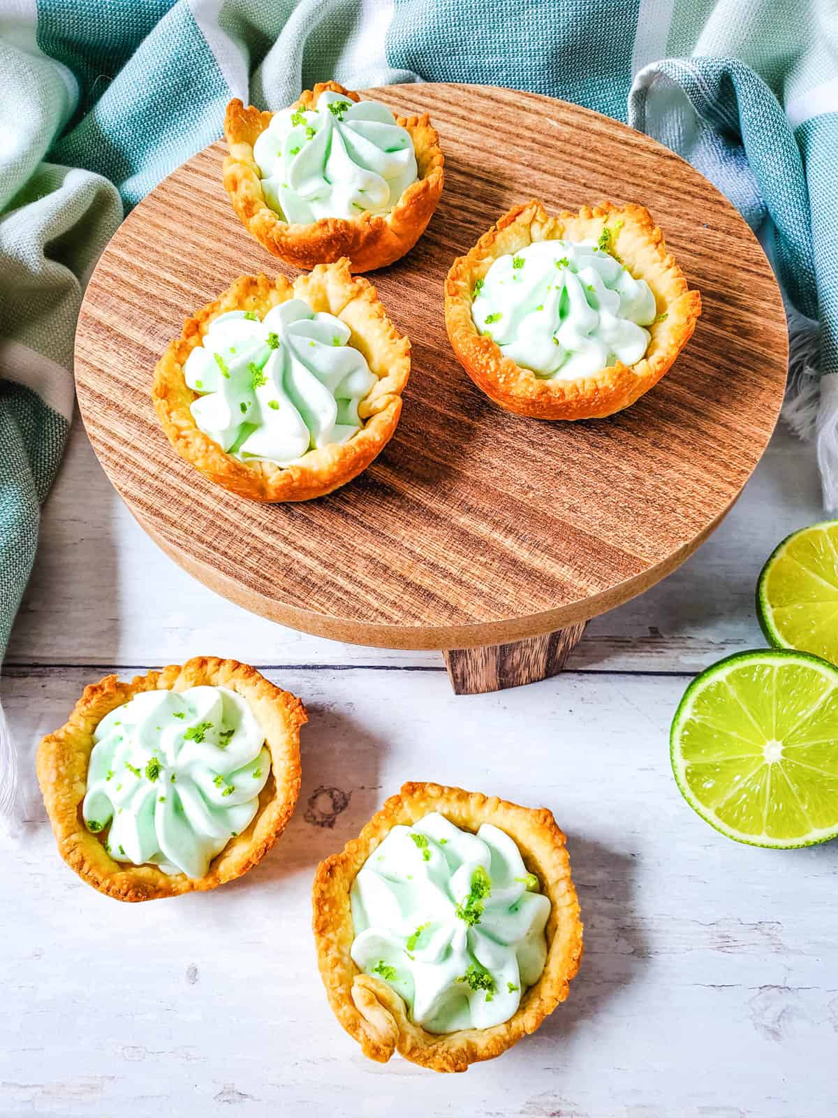 Three delicious key lime pie bites on a wooden plate, with another two beneath them on the table. 