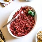 A white bowl with cream cheese cranberry jalapeno dip garnished with cilantro and a serving knife sticking out.