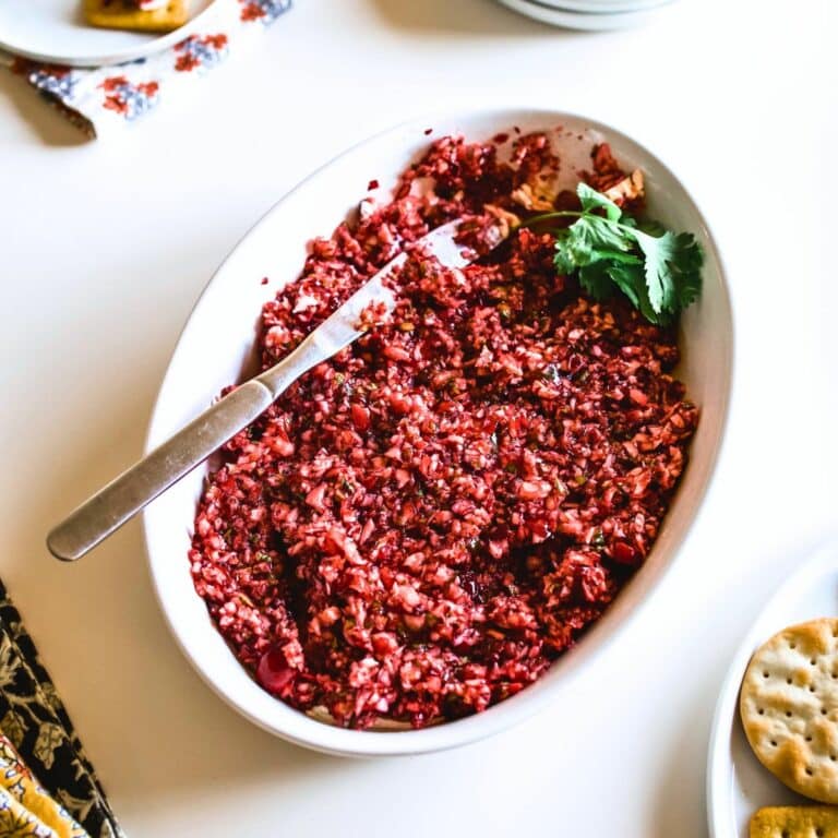 A white bowl with cream cheese cranberry jalapeno dip garnished with cilantro and a serving knife sticking out.