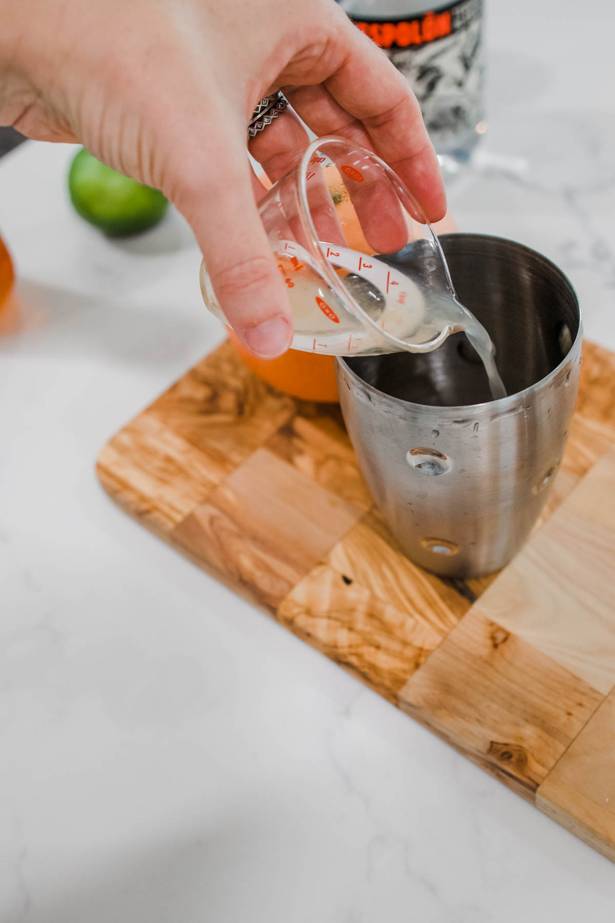 fresh lime juice A hand adding fresh lime juice to a cocktail shaker.
