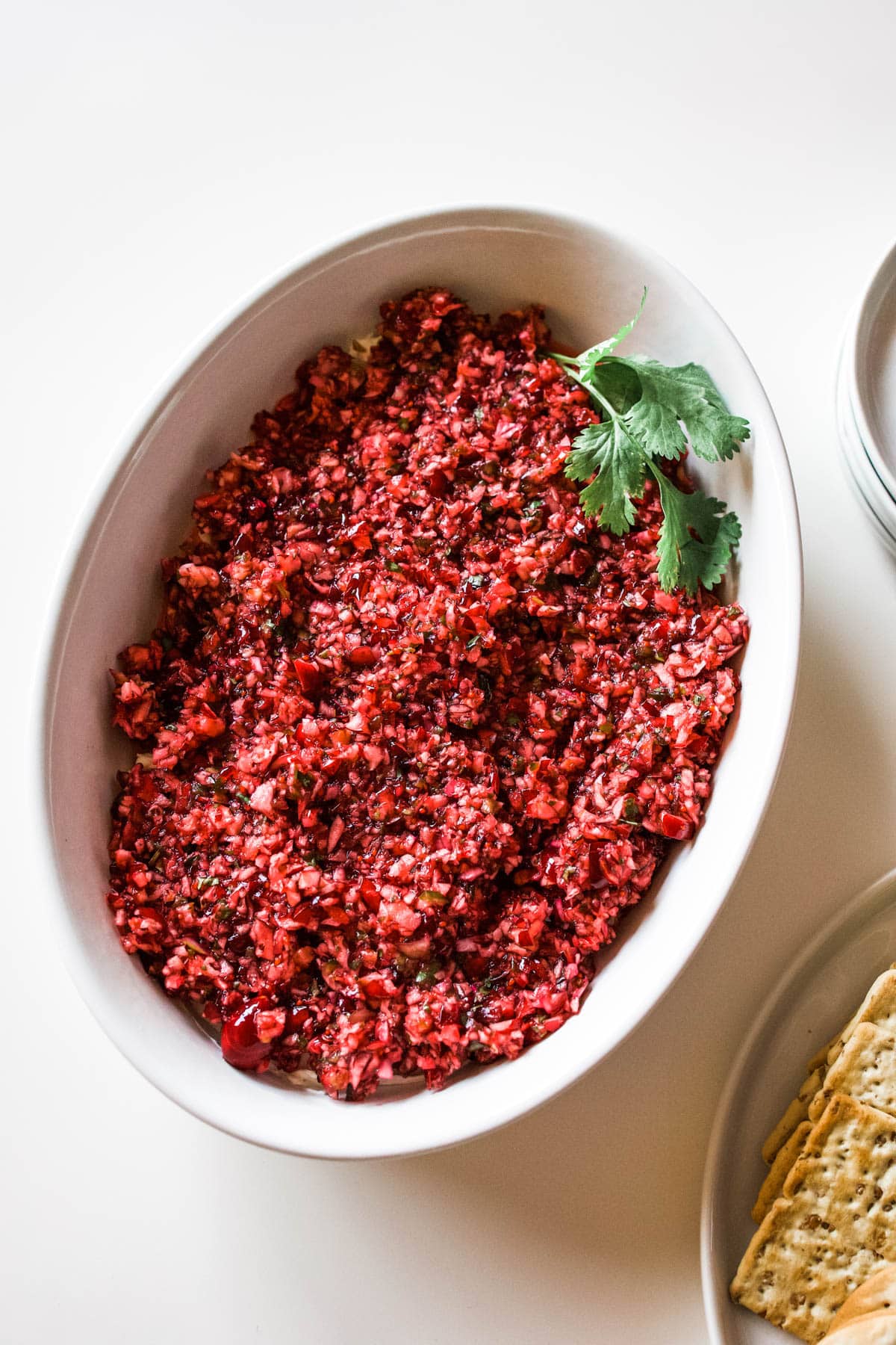 cranberry jalapeno dip recipe White dish holding cranberry jalapeno dip garnished with cilantro on a table.